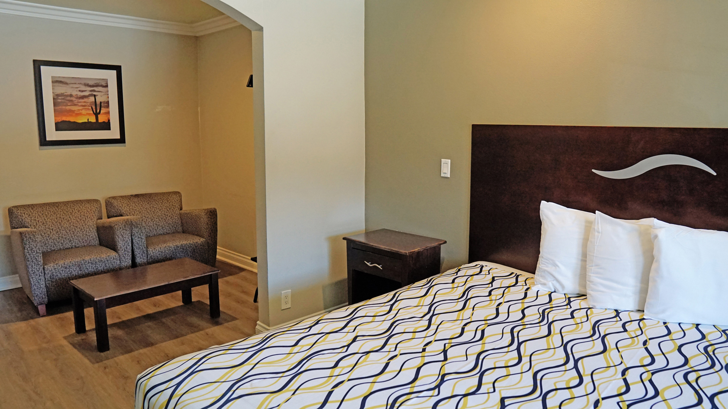 A hotel room with a bed, nightstand, seating area, and artwork on the wall.